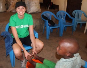 Dalice washing the feet of a young boy before fitting his new shoes, in Tanzania